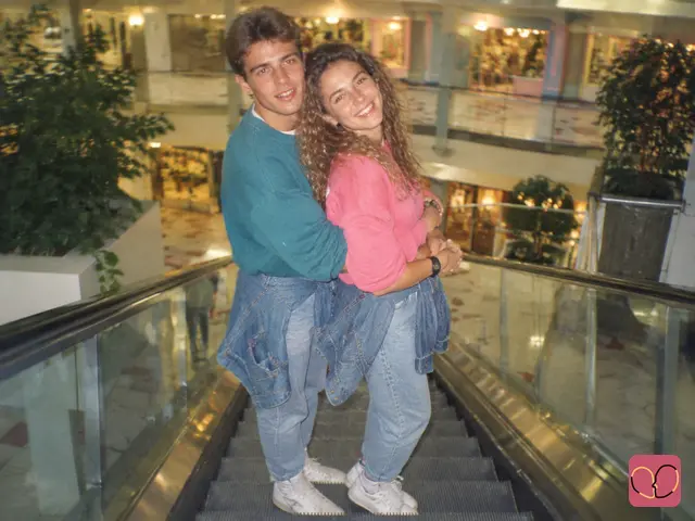 1980s couple photo — A couple hugs on a mall escalator, laughing at the camera